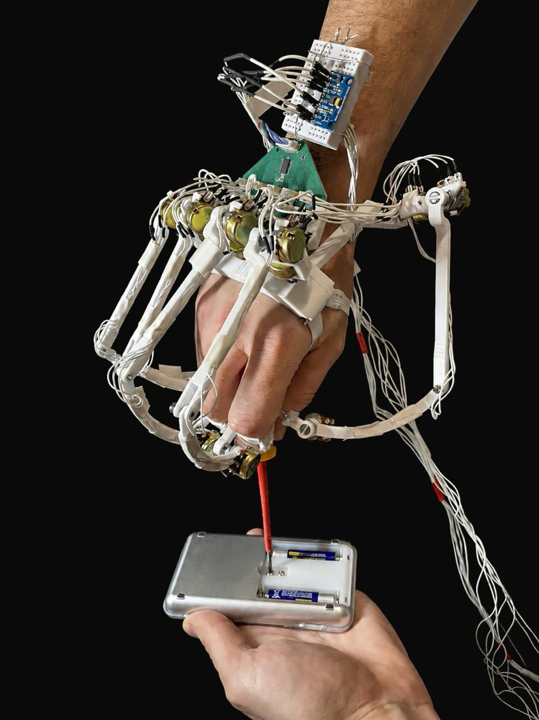 The instrumented glove worn on a hand driving a screwdriver into a device, a potentiometer at each finger joint and the board at the wrist